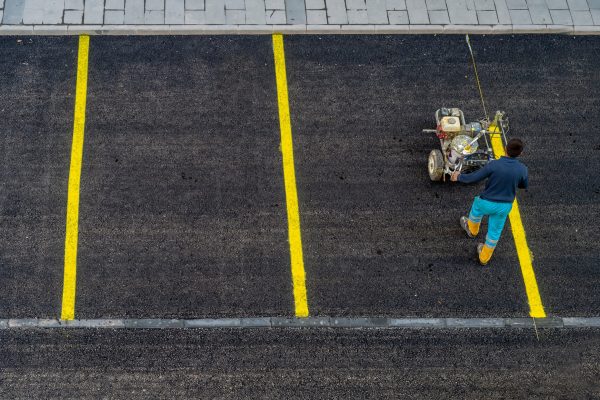 A worker is drawing outdoor concrete car parking lot is divided for making a slot for the park each car by a yellow line, with cement wheel coverings. in urban city.